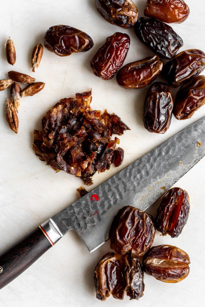 chopped and pitted dates on cutting board with chef knife.