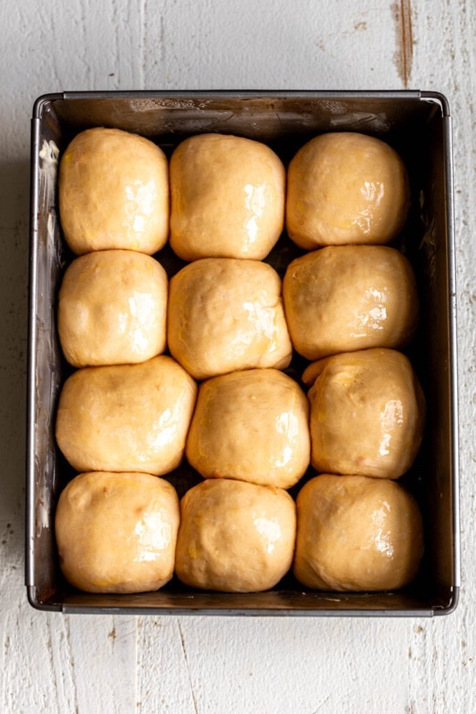 puffed divided sweet potato dinner roll dough balls in pan.