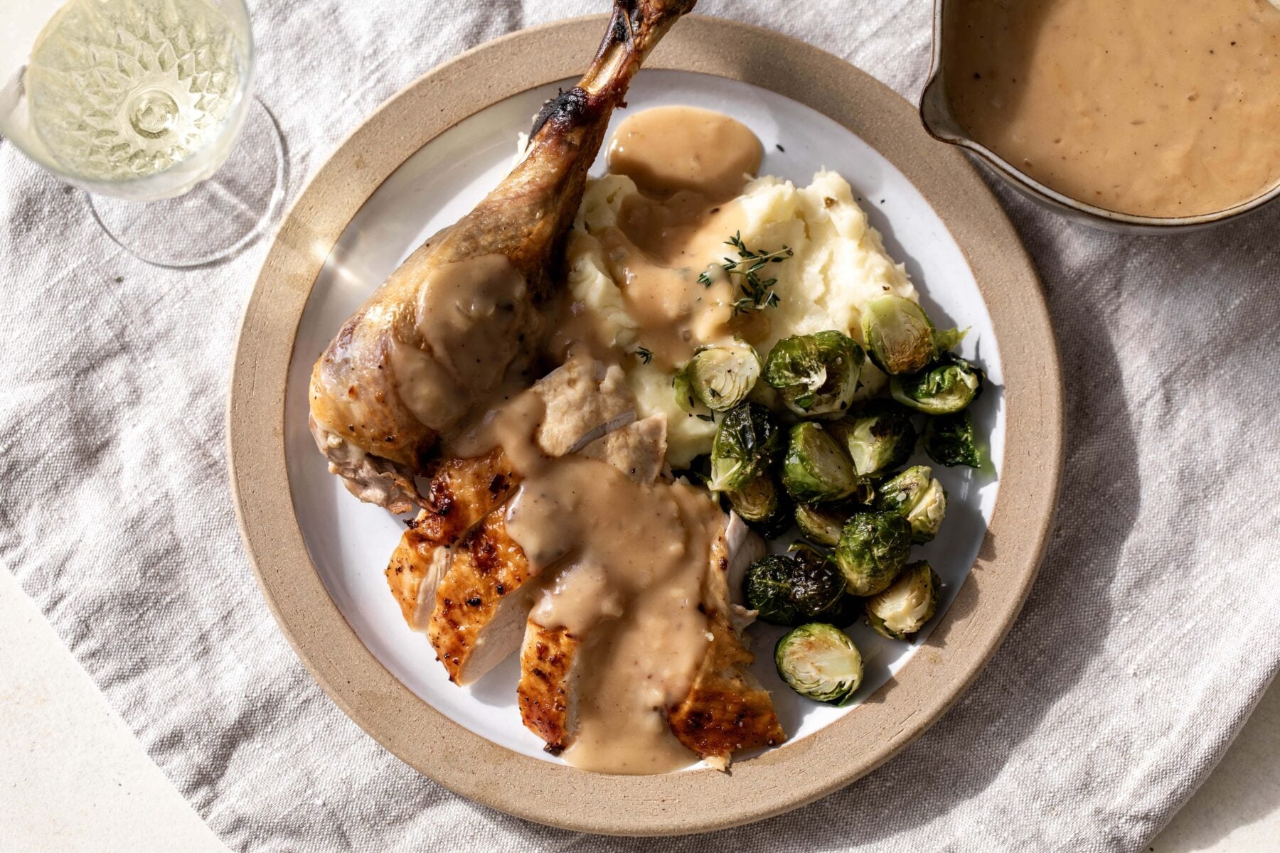 white wine gravy over turkey leg with mashed potatoes and brussels sprouts.