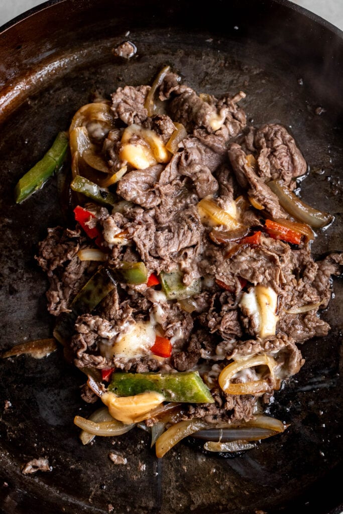 seared beef with onion and peppers in cast iron pan.