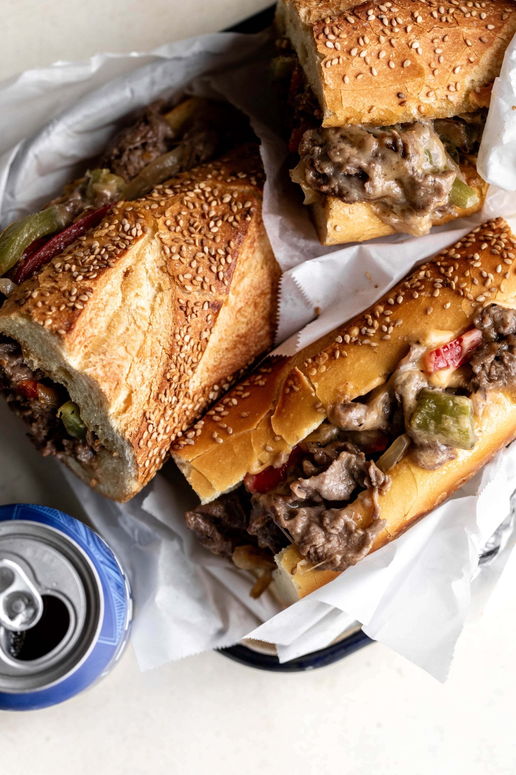 Philly cheesesteaks on sesame rolls with peppers and onions and a beer.