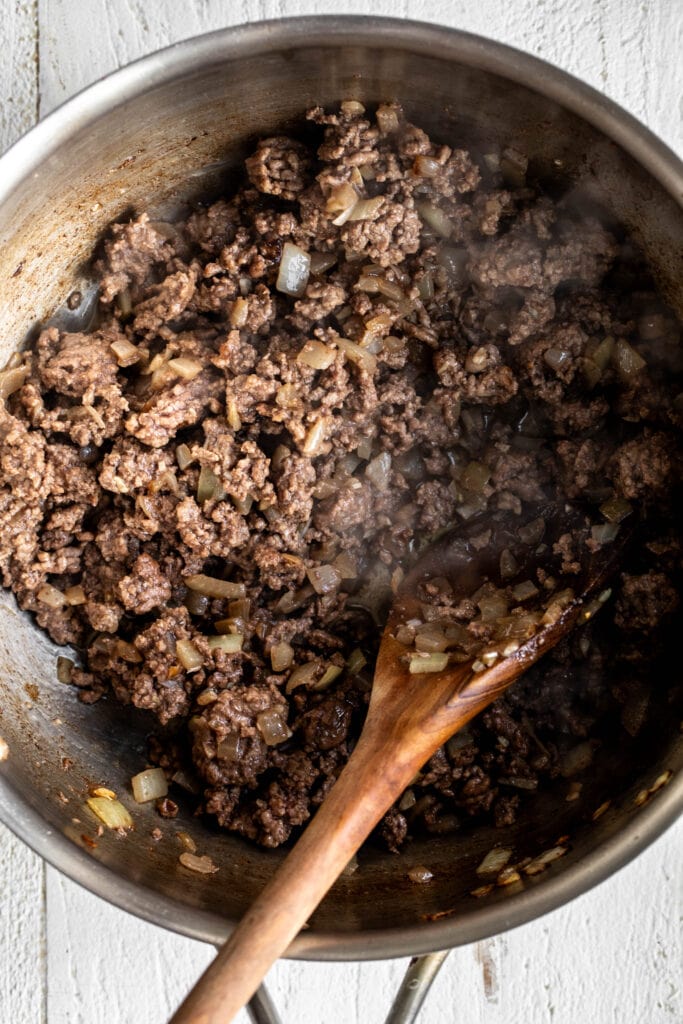 ground beef and sautéed onions with wooden spoon.