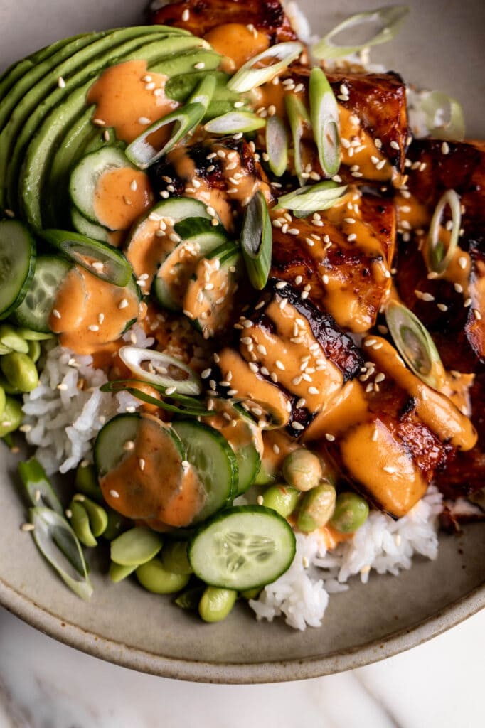 Teriyaki Salmon Bowls with Sriracha Cream Sauce over rice with cucumber.