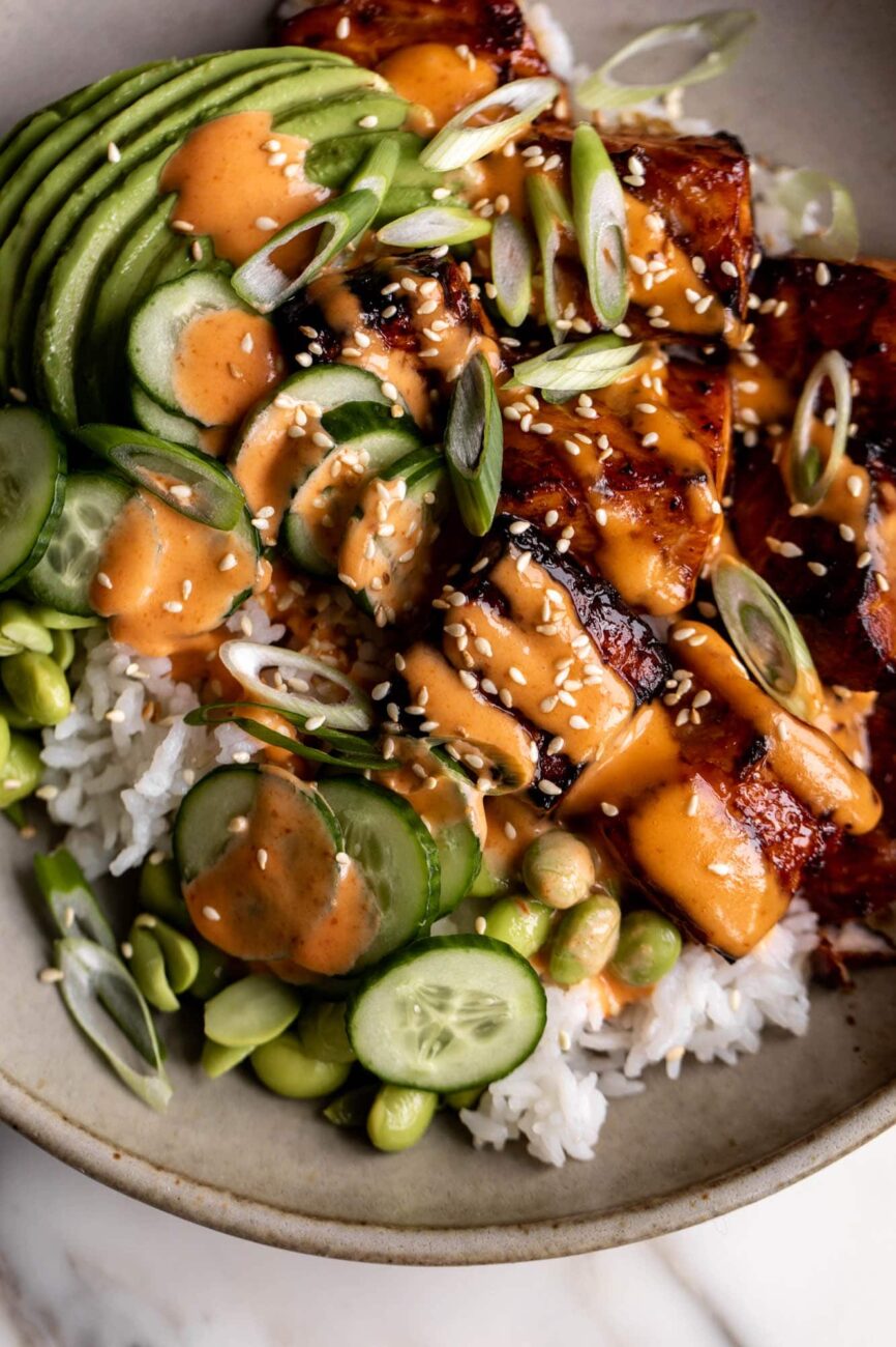 Teriyaki Salmon Bowls with Sriracha Cream Sauce over rice with cucumber.
