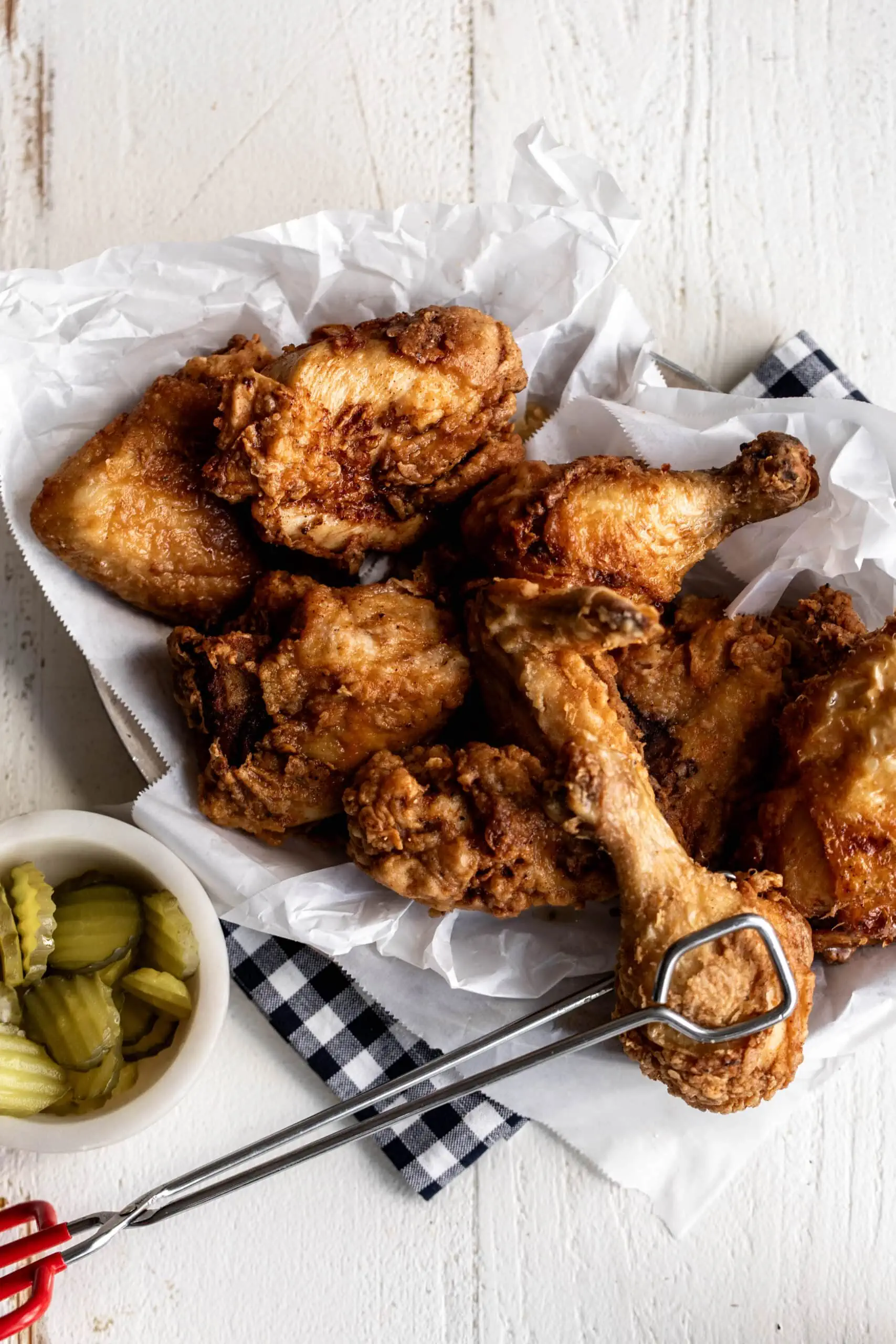 brined fried chicken drumsticks and thighs with a side of pickles and tongs.