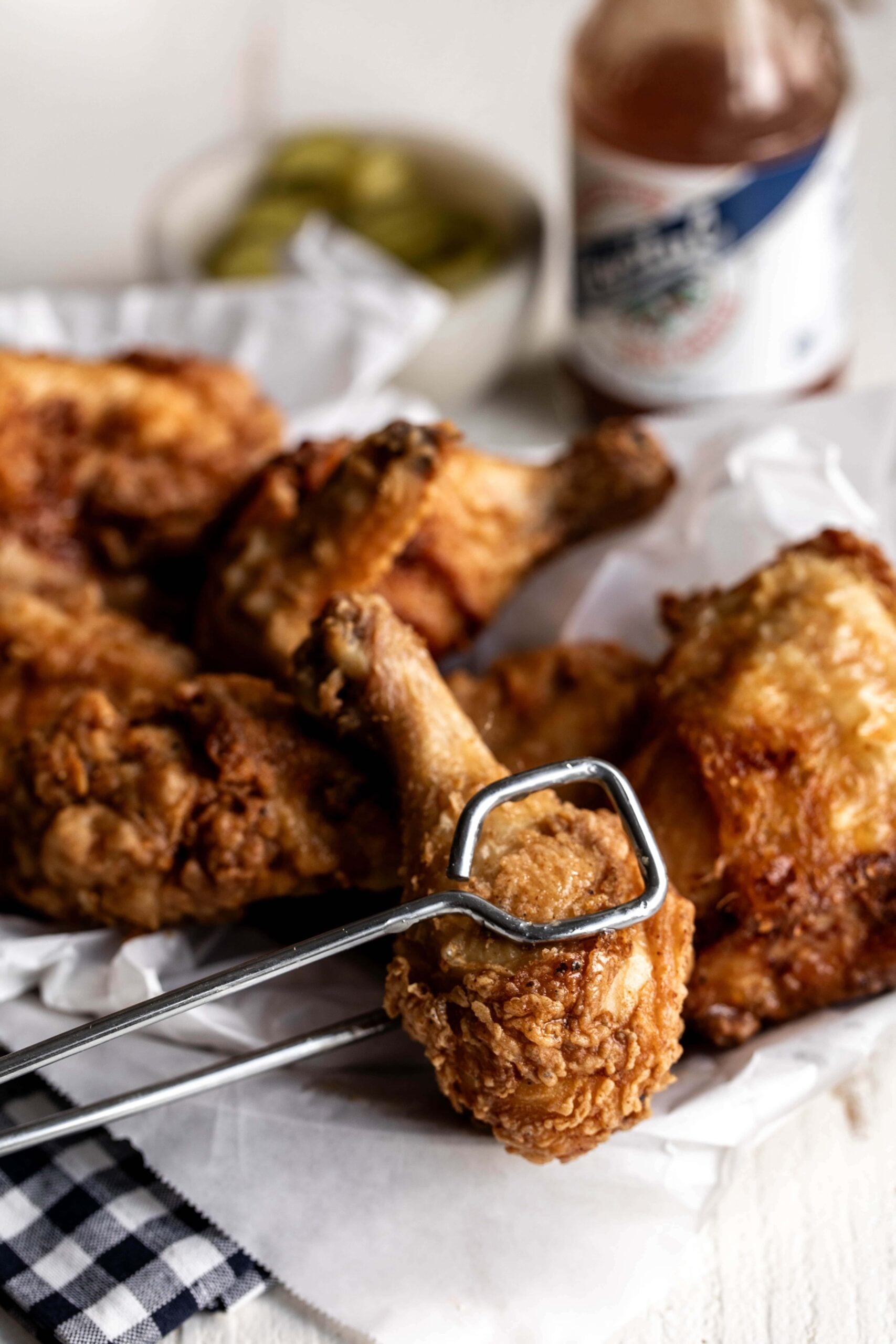 best brined fried chicken drumstick held with tongs.