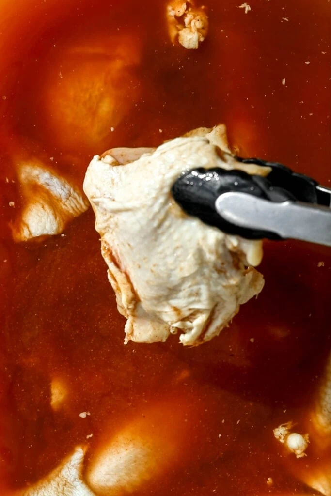 skin-on chicken thighs with tongs out of brine.