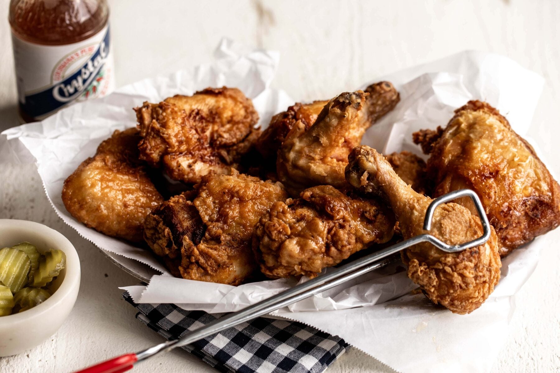 brined fried chicken drumsticks and chicken thighs on a silved platter with red tongs.