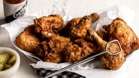 brined fried chicken drumsticks and chicken thighs on a silved platter with red tongs.