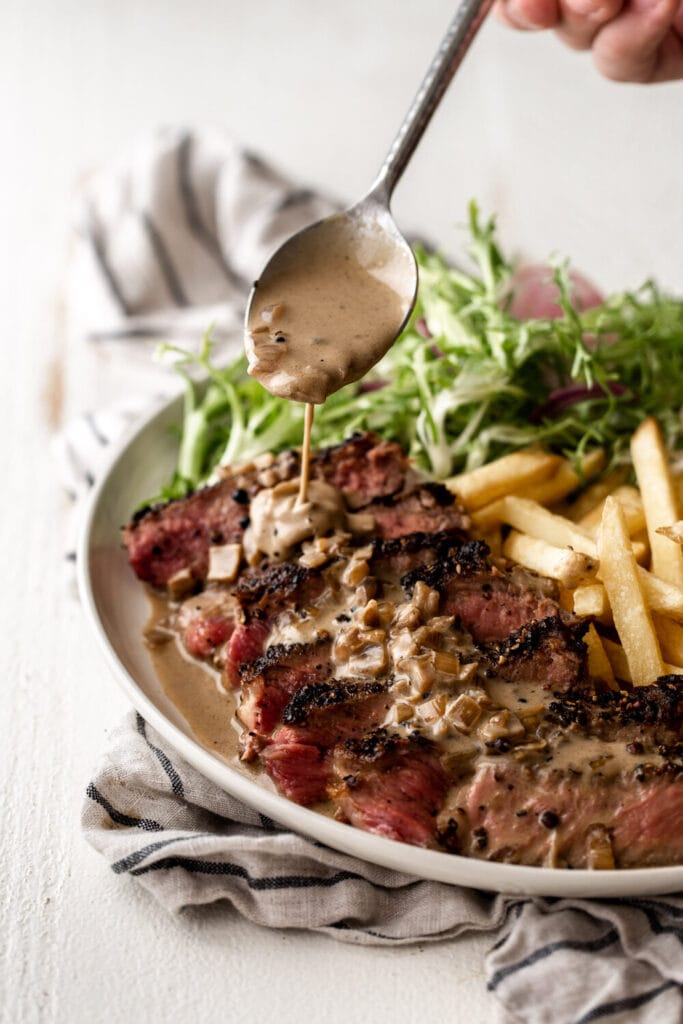 butter basted steak au poivre with french fries and side salad.