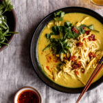 coconut turmeric chicken soup with cilantro and chili crisp with chopsticks.