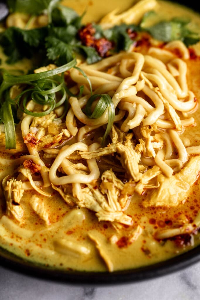 coconut turmeric chicken soup broth with noodles, green onion and cilantro leaves.