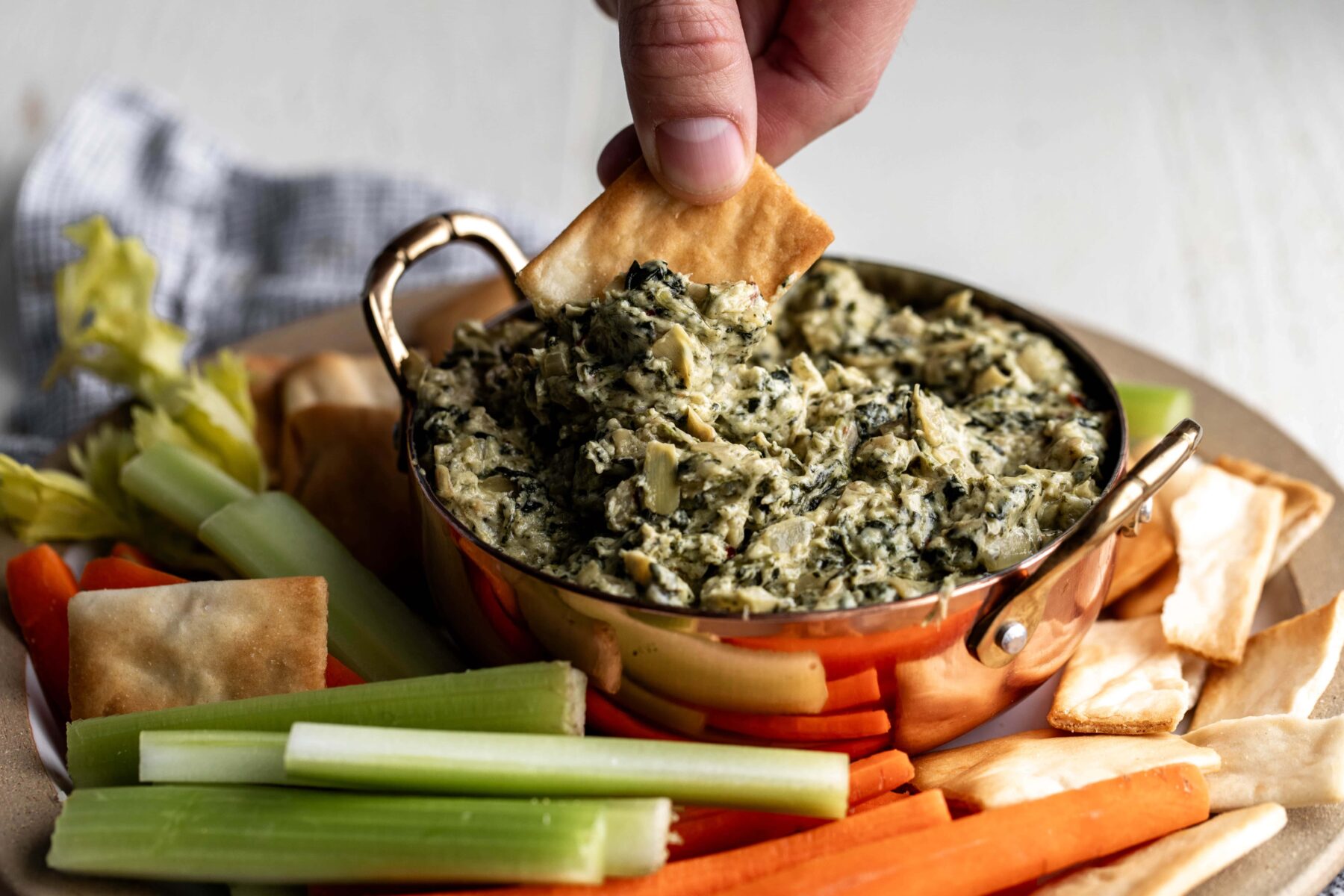 dipping pita chip in creamy spinach artichoke dip with celery and carrots.