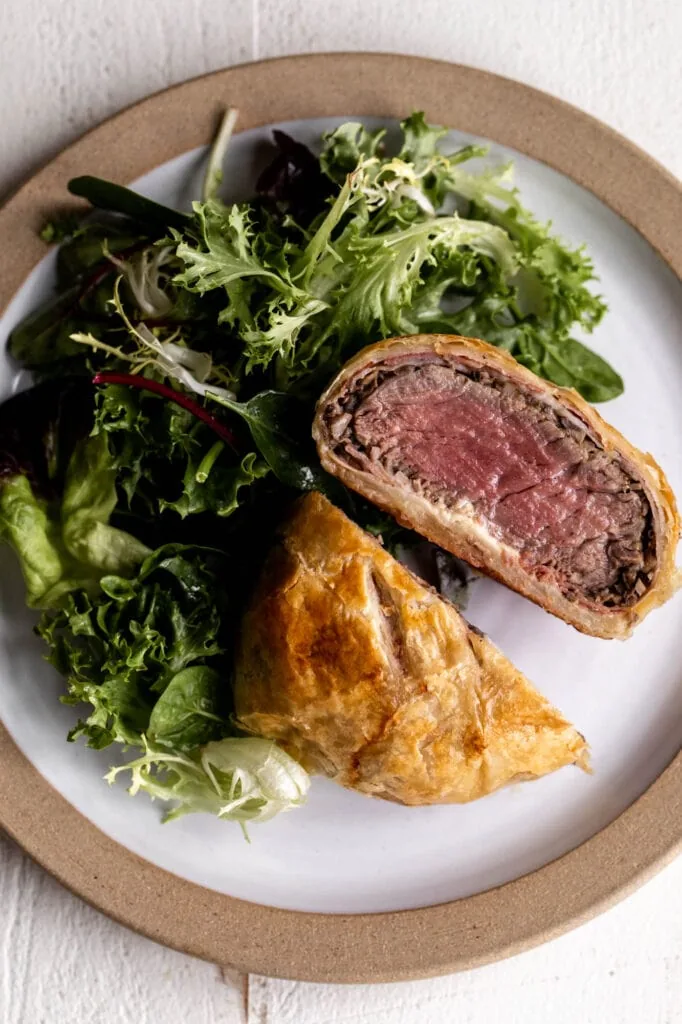 individual portions of beef wellington cut in half with leafy green salad