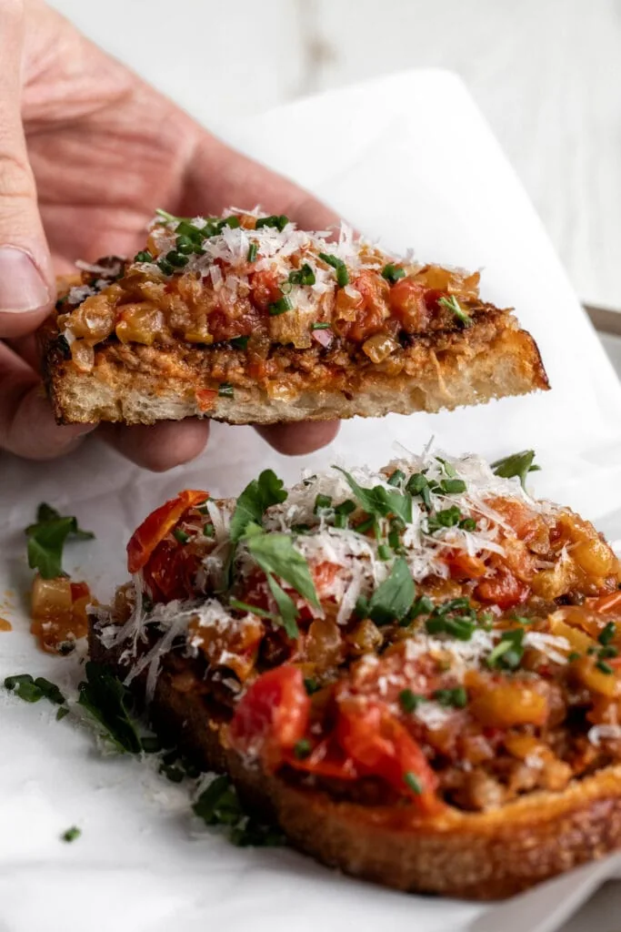 hand lifting sausage and peppers toast.