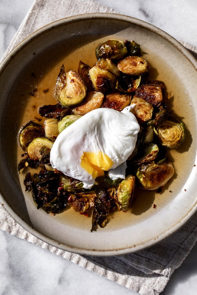 roasted brussels sprouts in a light bacon dashi broth with a poached egg split open in stone bowl