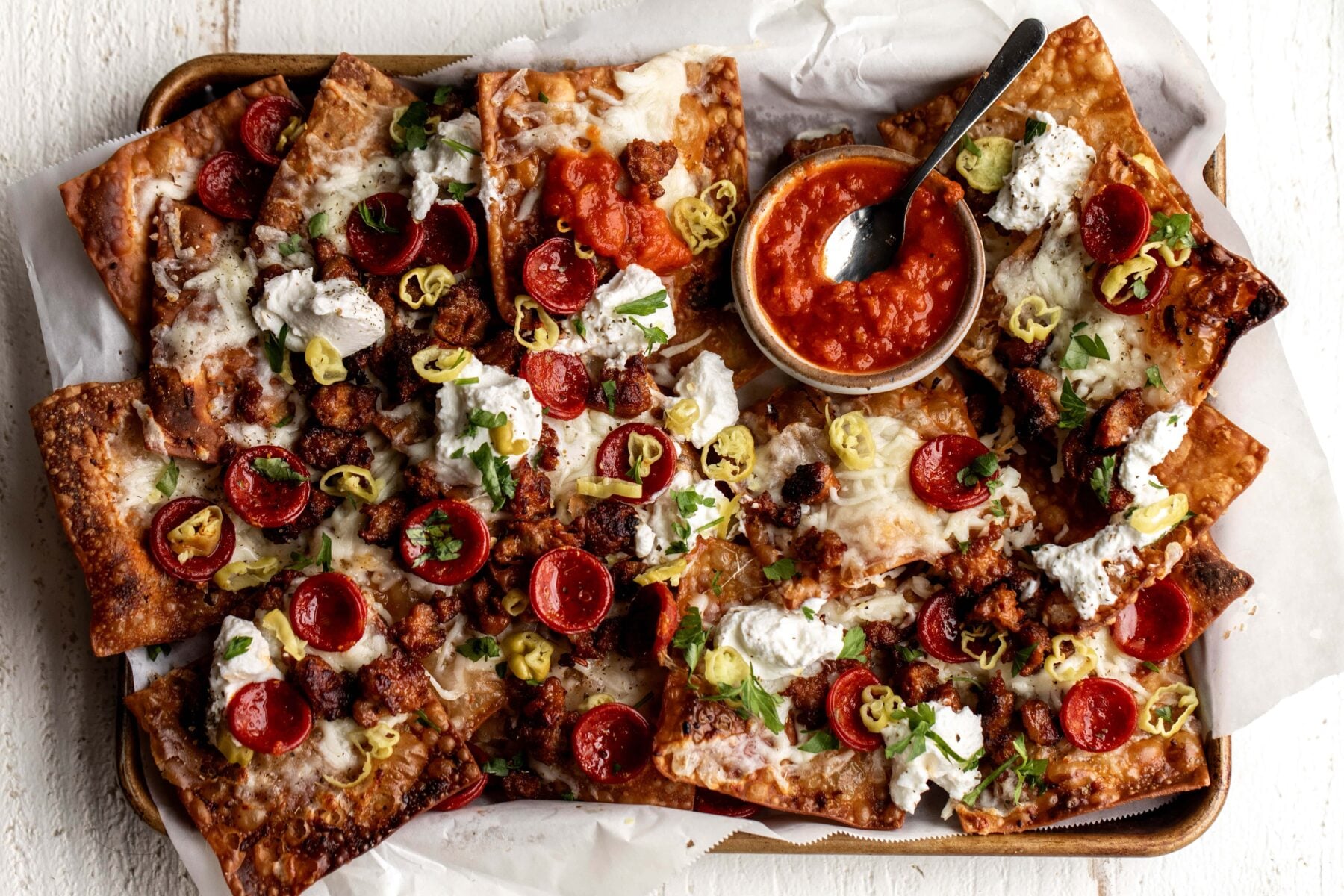 Italian nachos with marinara sauce, pepperoni and sausage on baking sheet.