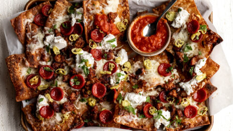 Italian nachos with marinara sauce, pepperoni and sausage on baking sheet.