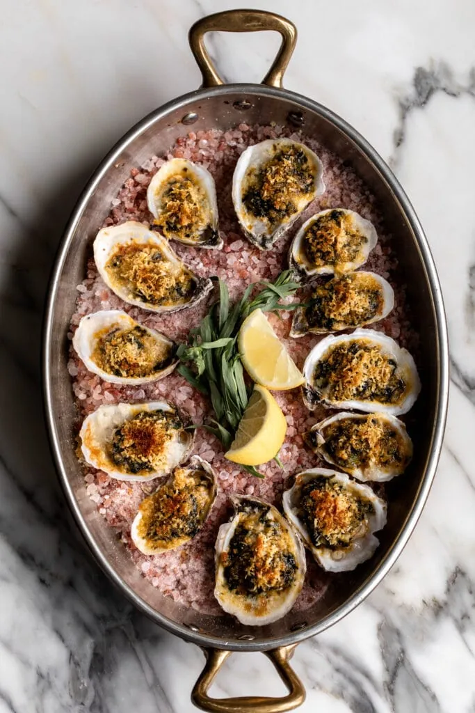 baked oysters rockefeller in baking dish with lemon wedges