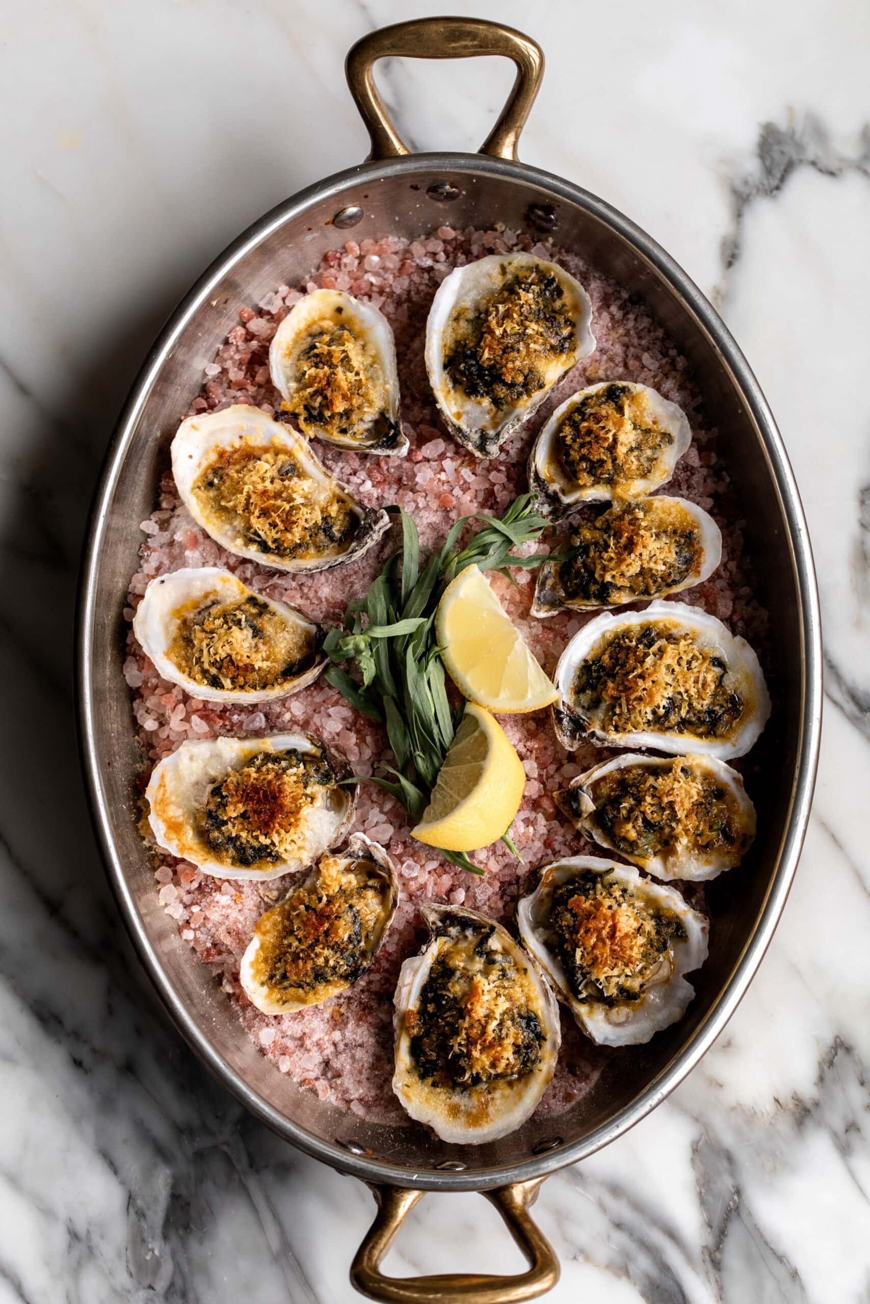 baked oysters rockefeller in baking dish with lemon wedges.