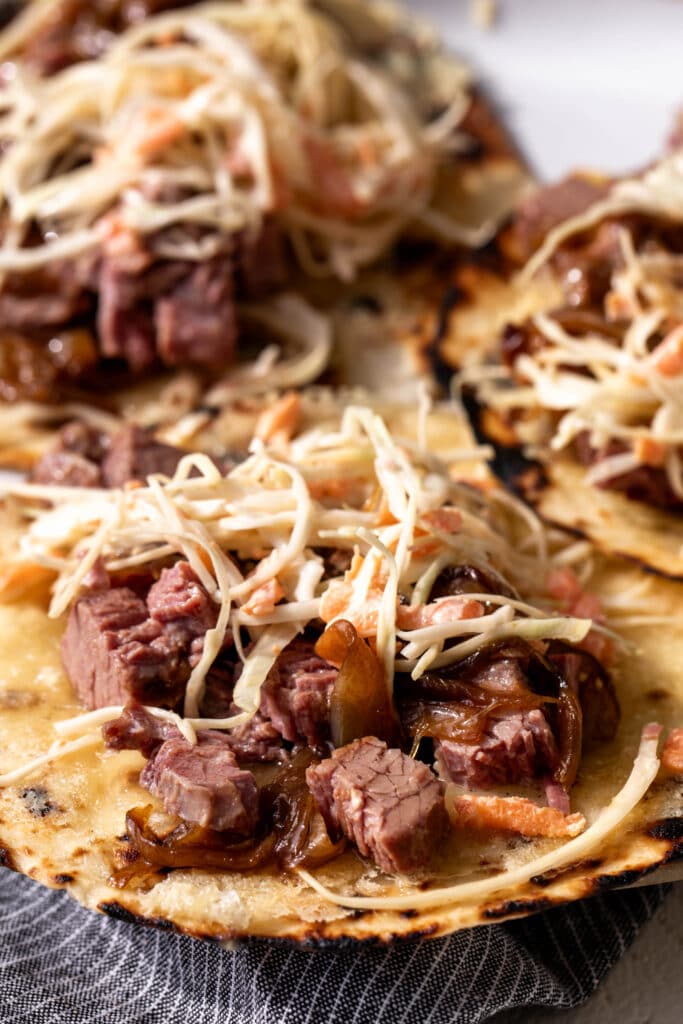 close up corned beef tacos with caramelized onions and creamy slaw on flour tortillas.
