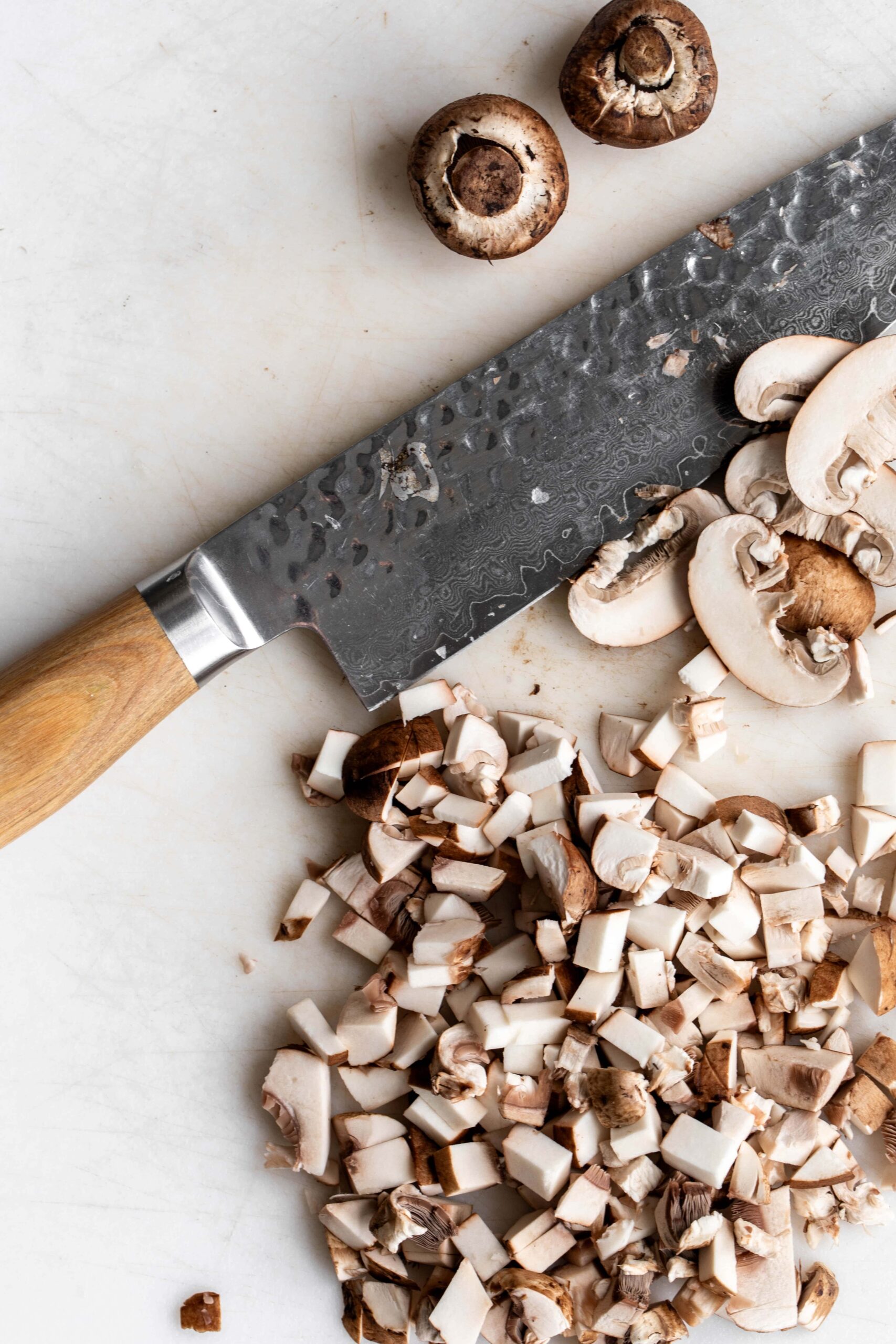 chopped baby bella mushrooms on cutting board with chef knife.