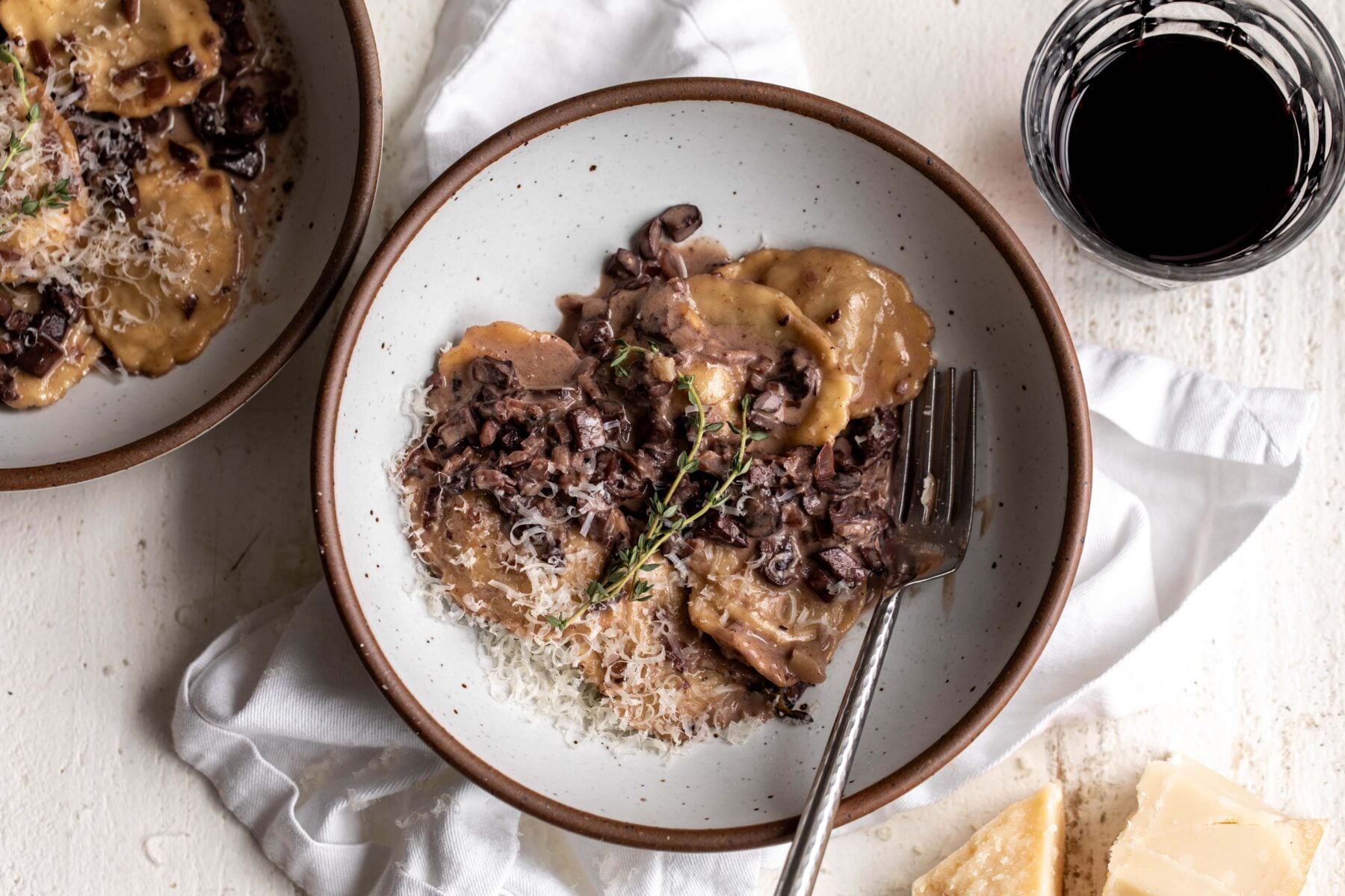 creamy mushroom ragu sauce with short rib ravioli with thyme sprig and parmesan.