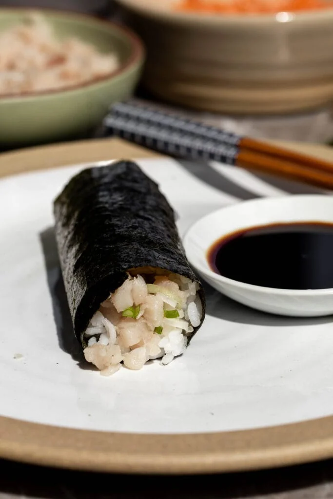 Finished yellowtail and green onion hand roll on plate with soy sauce. 