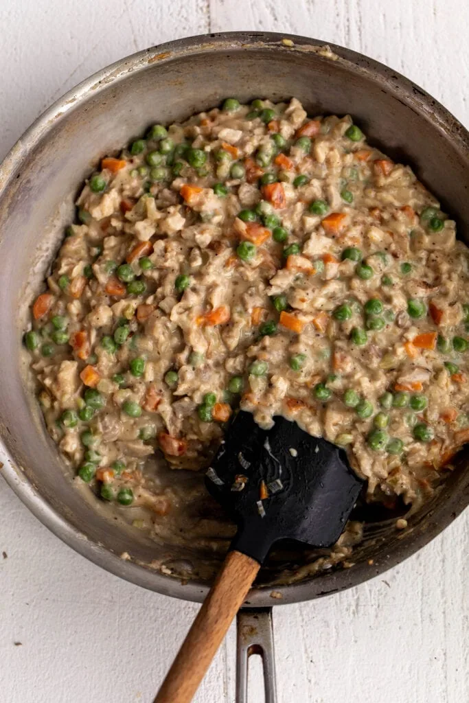 chicken pot pie croquette filling with carrots, peas and chicken in pot.