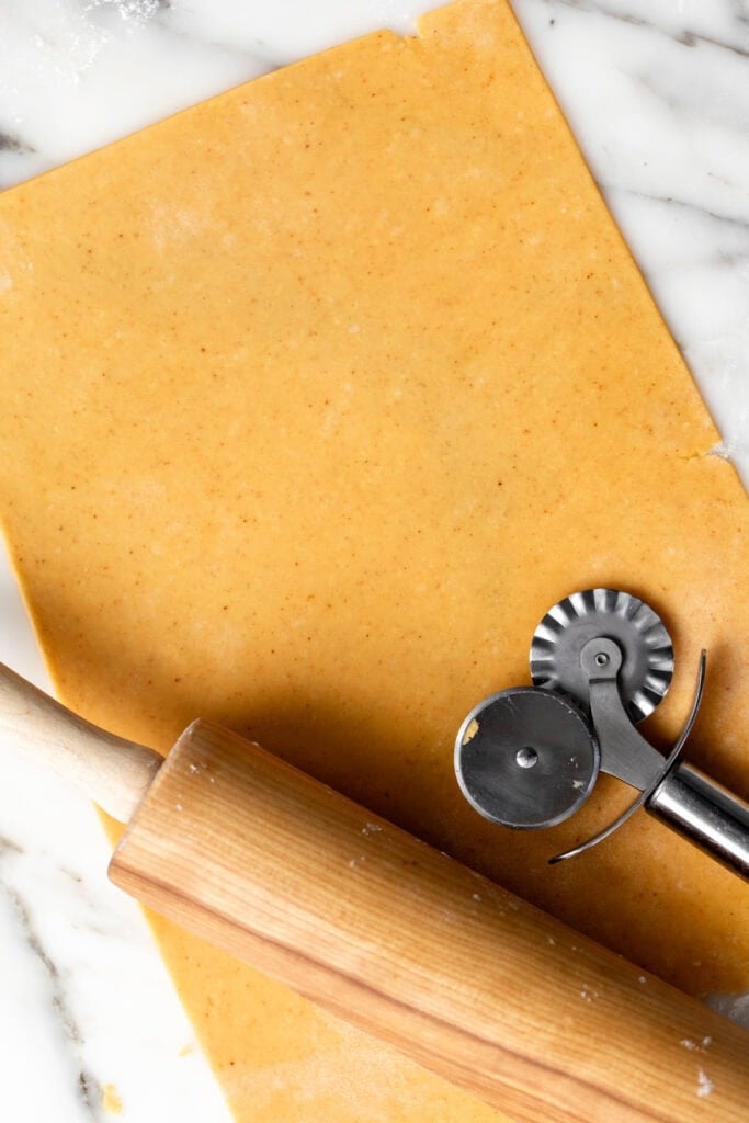 cheddar cracker dough rolled out with rolling pin and pastry cutter on marble.