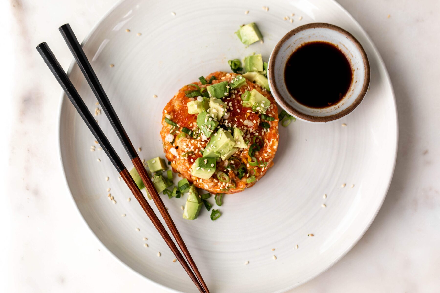 salmon tartare with diced avocado and green onion with chopsticks and soy sauce.