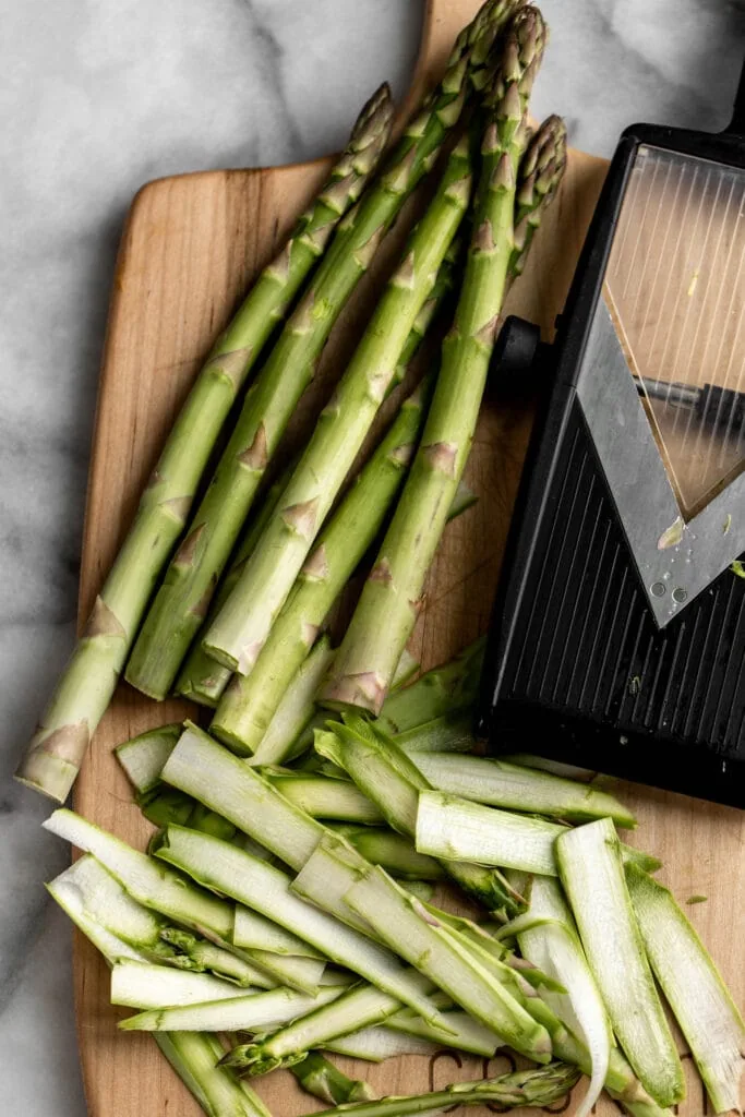 shaved asparagus stalks on cutting board with mandolin.