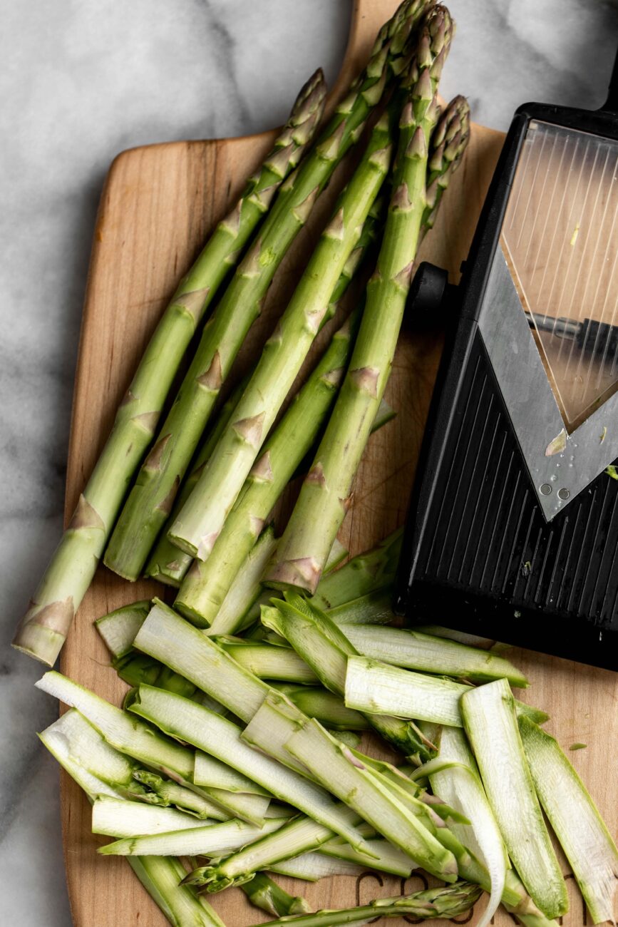 shaved asparagus stalks on cutting board with mandolin.