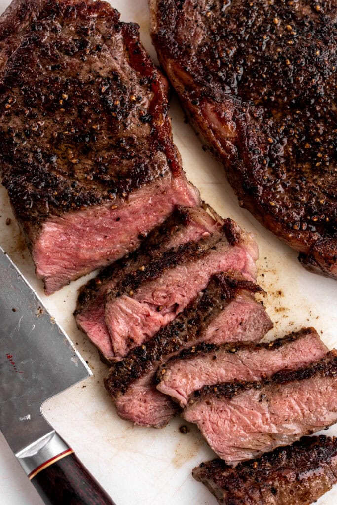 Cooked and sliced ribeye steak on cutting board ready for serving.