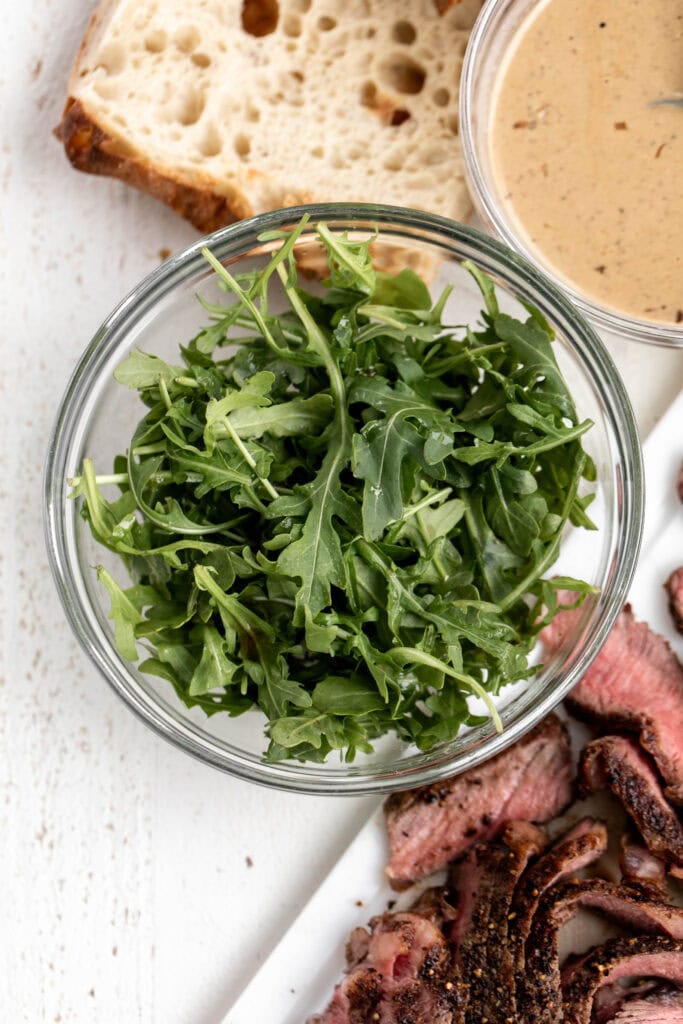 Fresh arugula in bowl with other sandwich ingredients ready for assembly.