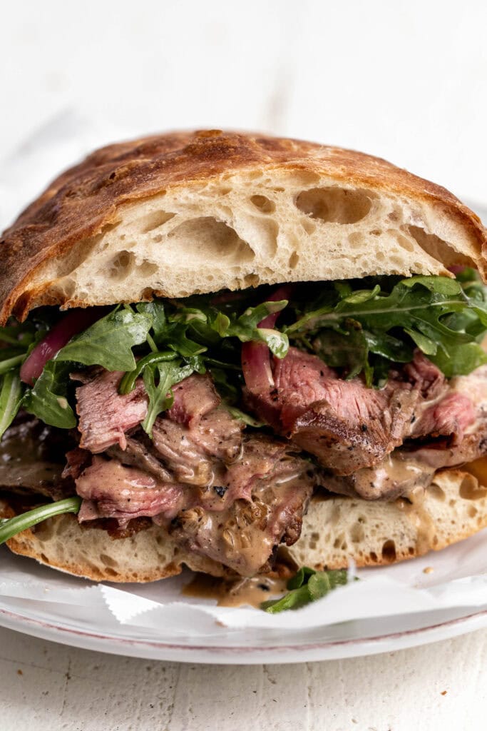 Finished steak au poivre sandwich with arugula on ciabatta bread. 