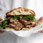 Steak Au Poivre sandwich with arugula on ciabatta on plate.