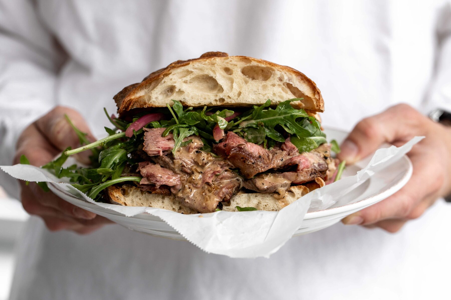 Steak Au Poivre sandwich with arugula on ciabatta on plate.