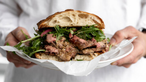 Steak Au Poivre sandwich with arugula on ciabatta on plate.