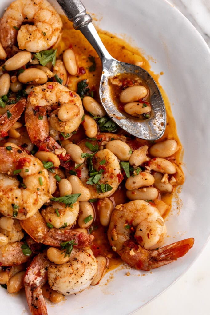 spicy calabrian chili shrimp with white beans garnished with parsley.