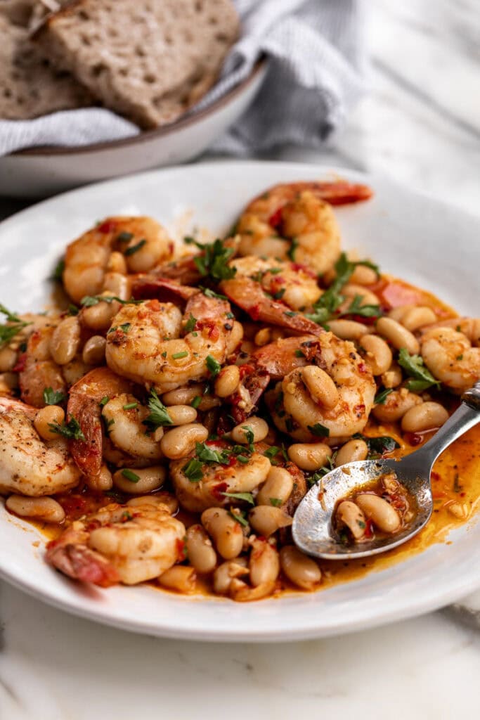 spicy calabrian chili shrimp with white beans garnished with parsley.