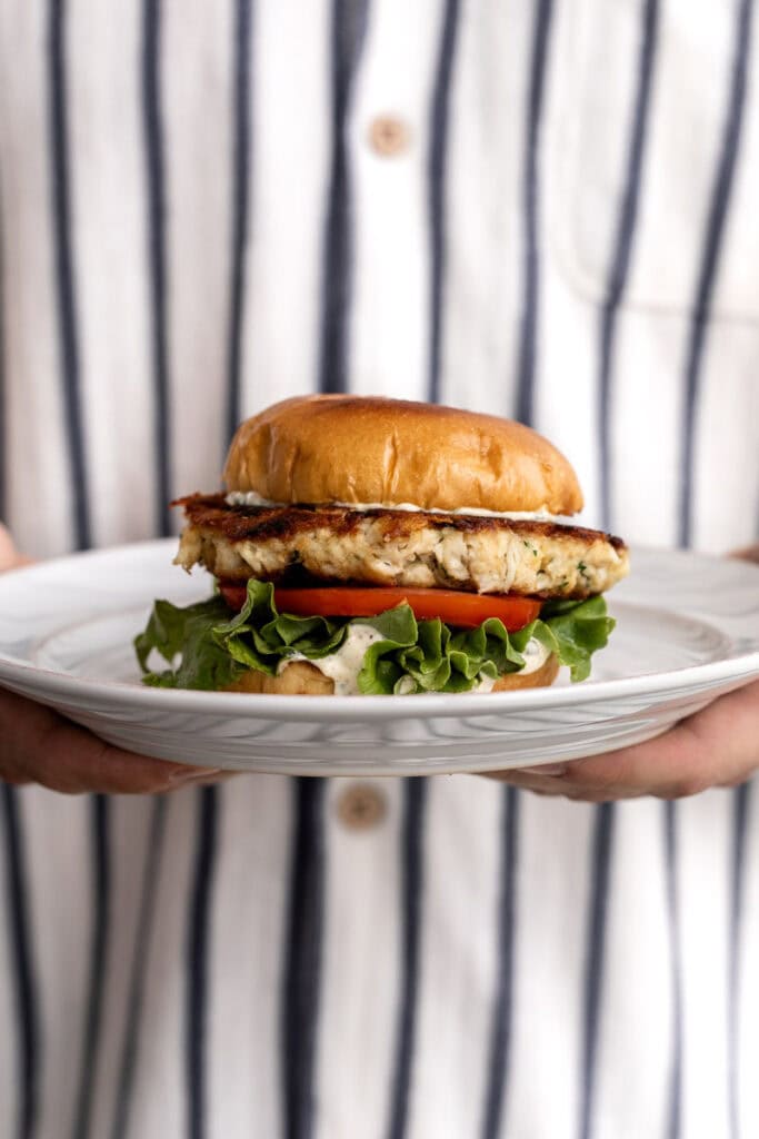 crab cake sandwich with green leaf lettuce and tomato on brioche bun.
