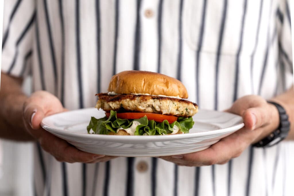 crab cake sandwich with green leaf lettuce and tomato on brioche bun.