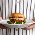 crab cake sandwich with green leaf lettuce and tomato on brioche bun.