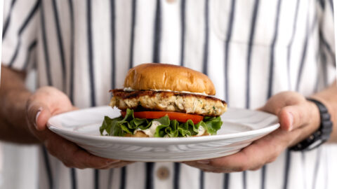 crab cake sandwich with green leaf lettuce and tomato on brioche bun.