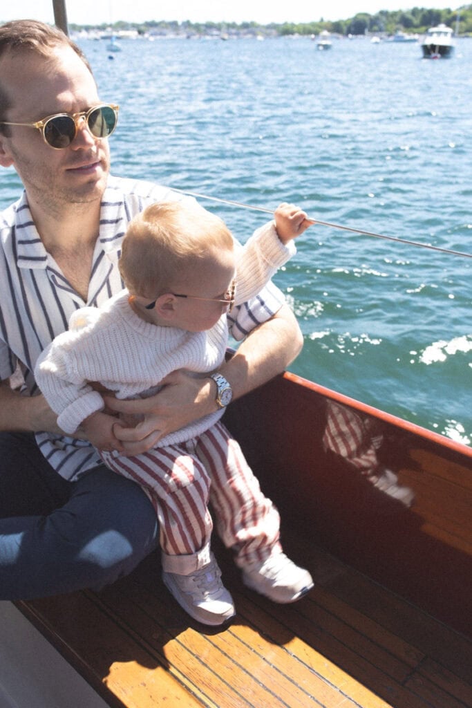 holding baby on boat in red striped pants.