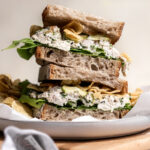 herbed chicken salad sandwich on sourdough bread topped with lettuce, pickles and chips.