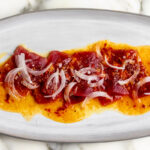 orange calabrian chili tuna crudo topped with shaved onion on oval plate.