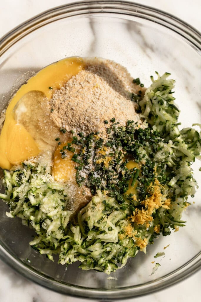 zucchini fritters ingredients in glass mixing bowl.