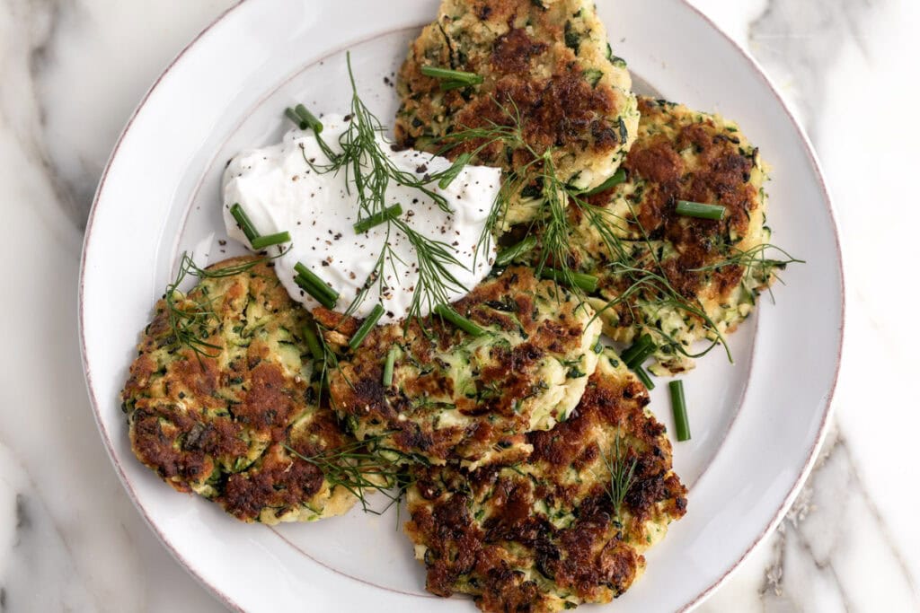 zucchini fritters with lemon yogurt sauce garnished with chopped chives and dill.